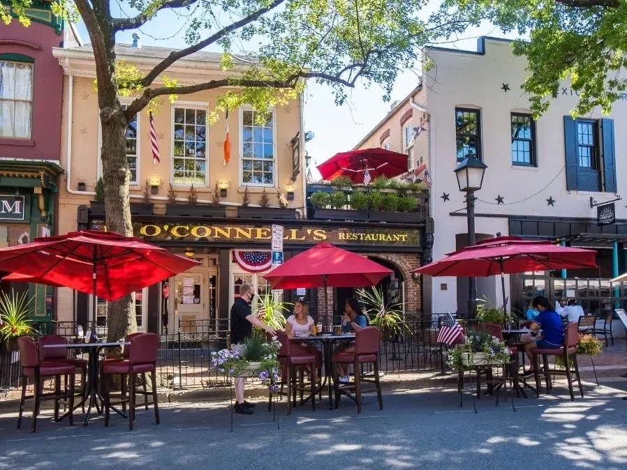 Restaurant sidewalk sale setup with red umbrellas and customers dining outdoors