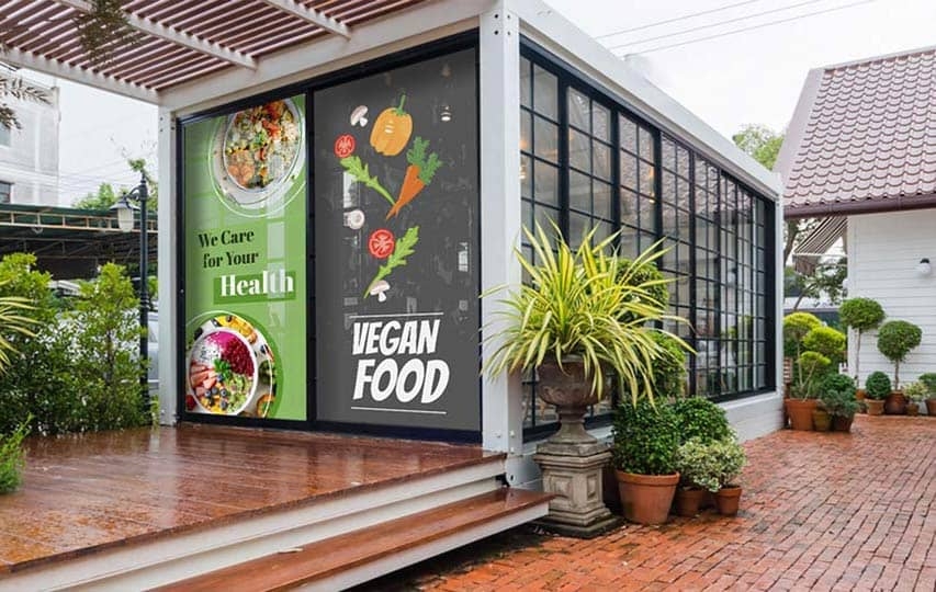 Vegan restaurant storefront with window decals and potted plants