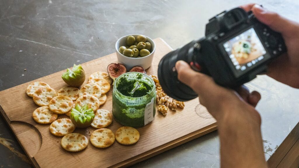 Fotógrafo capturando una tabla de aperitivos con crackers, pesto, aceitunas y frutas en un restaurante.