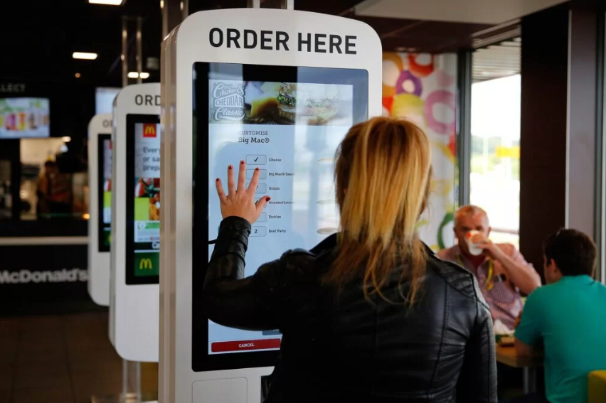Woman placing an order at a self-service touchscreen kiosk in a fast-food restaurant.