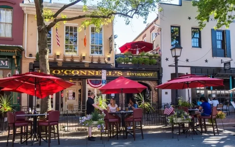 Restaurant sidewalk sale setup with red umbrellas and customers dining outdoors