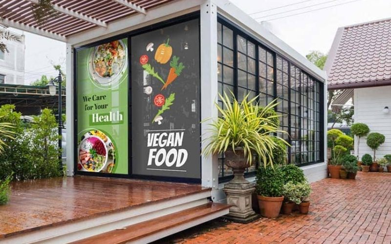 Vegan restaurant storefront with window decals and potted plants